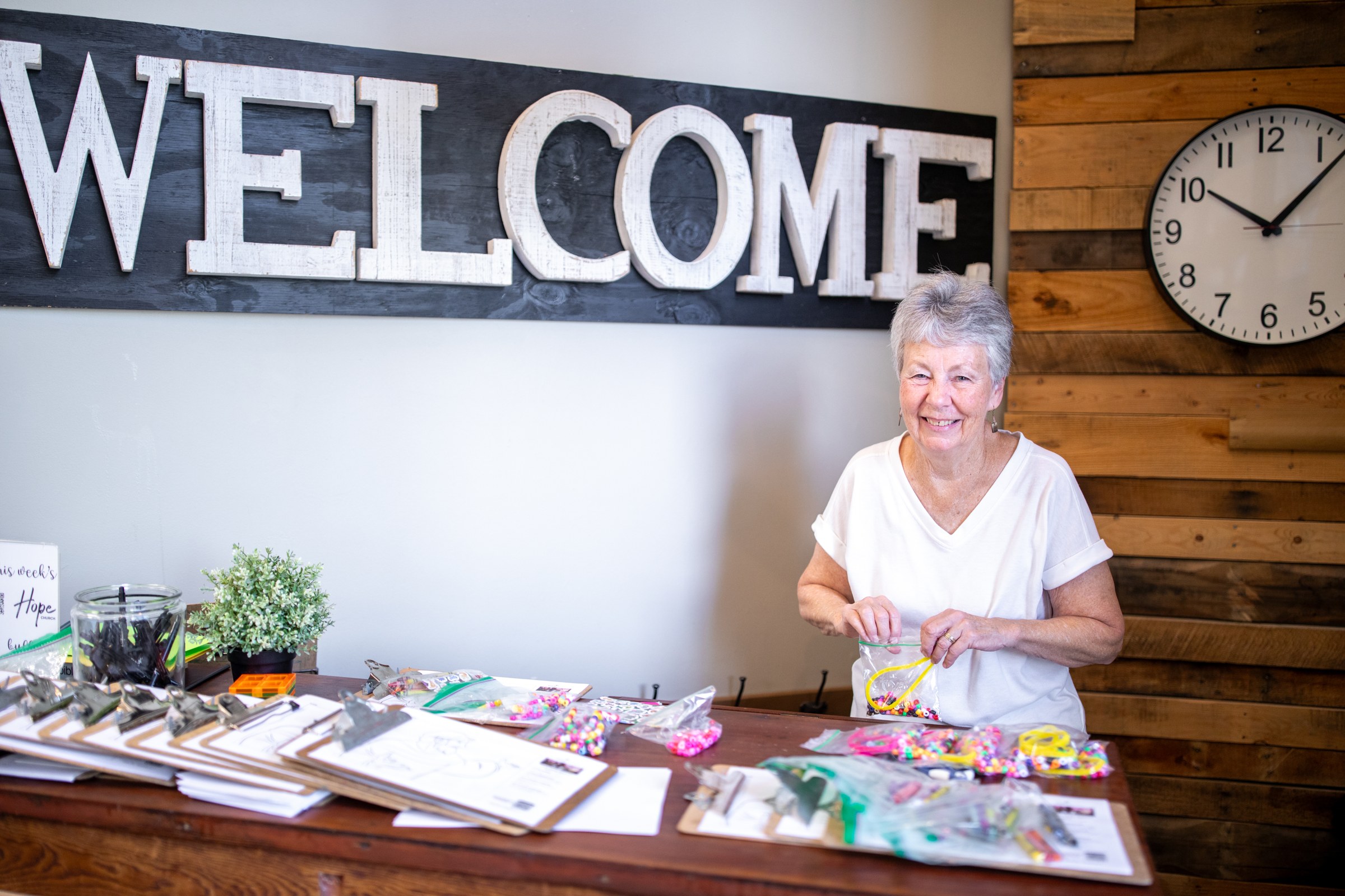 A smiling volunteer at the welcome table beneath a large WELCOME sign